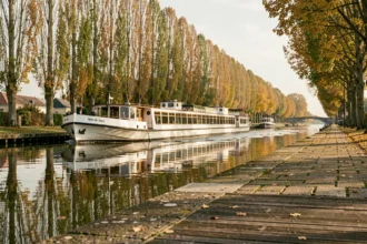 Péniche de croisière fluviale naviguant sur un canal bordé de peupliers en Hauts-de-France en automne