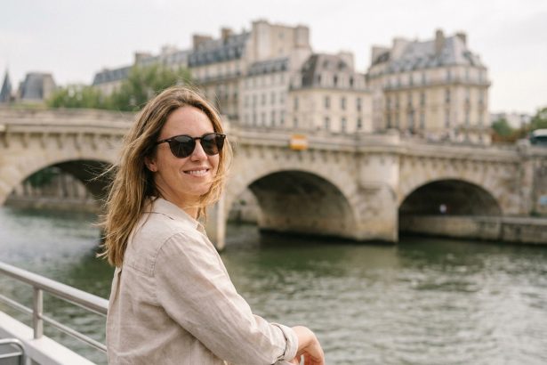 Femme souriante appuyée sur le bastingage d'un bateau sur la Seine avec le Pont Neuf en arrière-plan à Paris