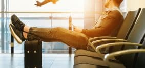 man sitting on gang chair with feet on luggage looking at airplane